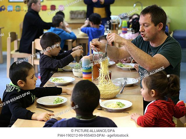 12 February 2019, North Rhine-Westphalia, Aachen: Children eat with the educator Guido Thissen (r) in the day care centre ""RoKoKo""