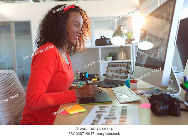 Happy female graphic designer using graphic tablet at desk