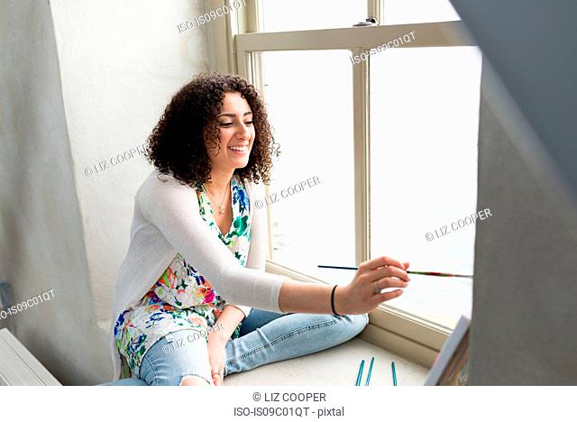 Young female painter painting canvas on studio windowsill