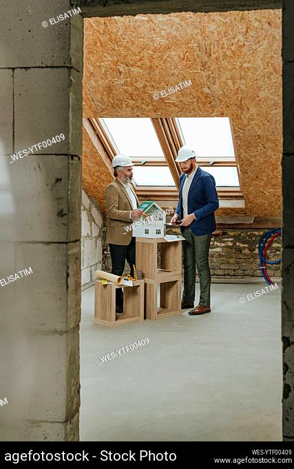 Architect explaining to colleague over house model seen through doorway
