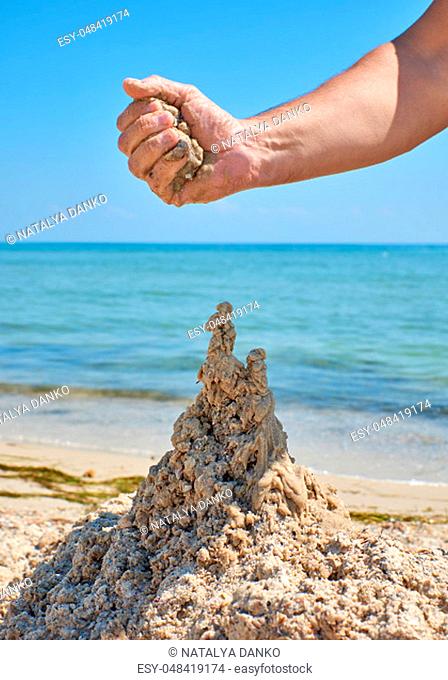 hand builds a castle from the wet sea sand on the beach on a summer day
