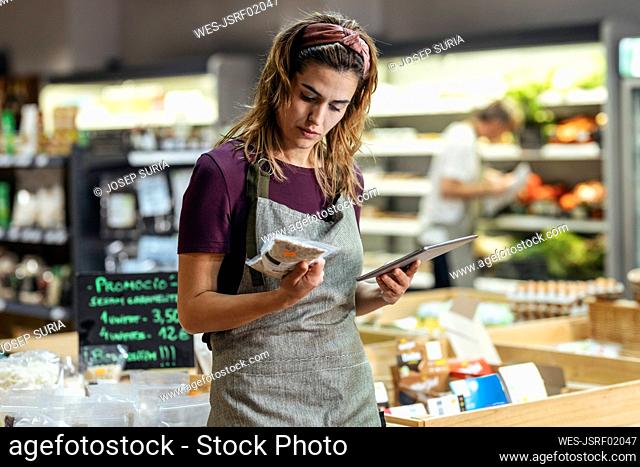 Shop owner holding tablet PC analyzing product at organic market