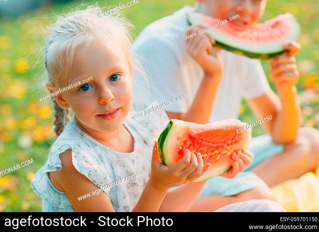 Funny little toddler kids brother and sister eating watermelon on the park. Happy boy and girl together. Childhood, Family, Healthy Diet Concept