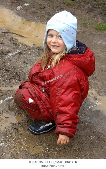 Child is playing during bad weather and rain in puddle and mud sludge