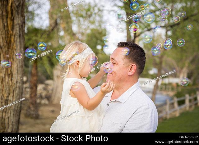 Affectionate father holding cute baby girl enjoying bubbles outside at the park