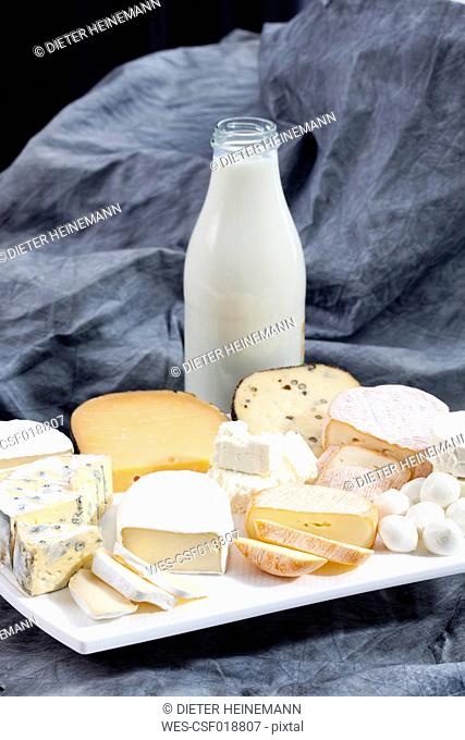 Varieties of cheeses on chopping board with bottle of milk on textile