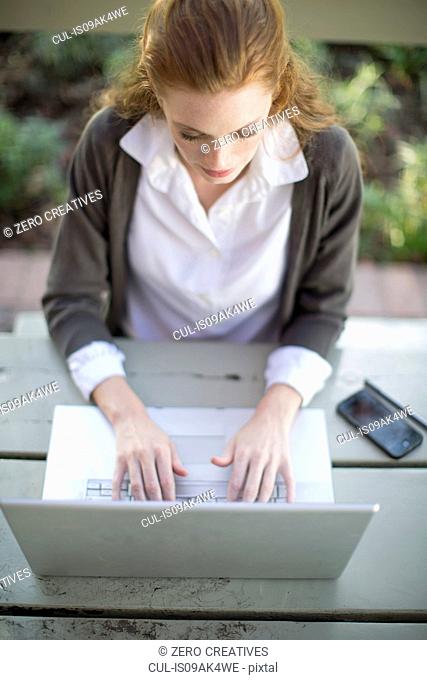 Young businesswoman typing on laptop at garden table