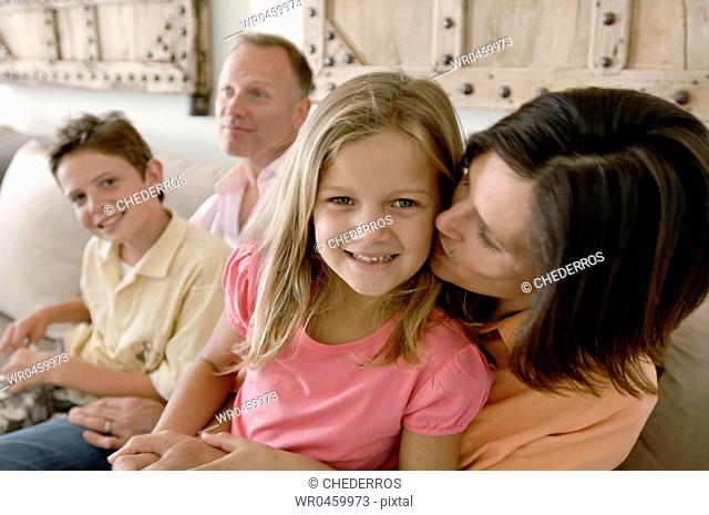 Close-up of a mature woman kissing her daughter with a mature man and his son sitting behind them