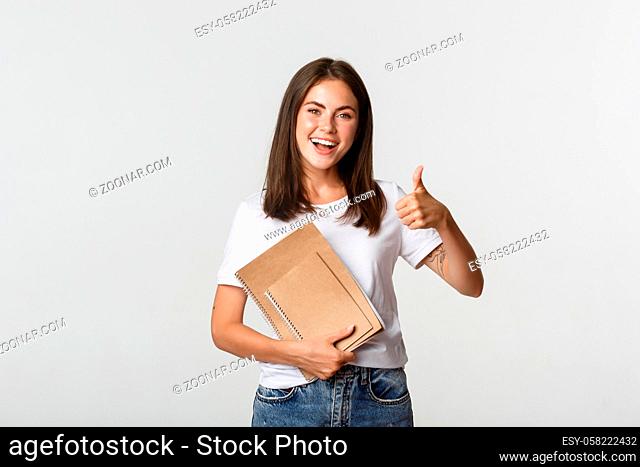 Cheerful smiling girl holding notebooks and showing thumbs-up, recommend courses or school