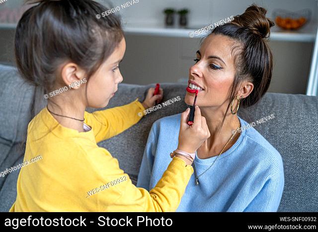Daughter applying red lipstick to mother in living room at home