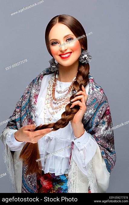 Happy beautiful young russian woman with very long braid in traditional shawl. Red lips. Over grey background