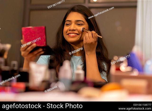 Young woman doing her make up in front of mirror