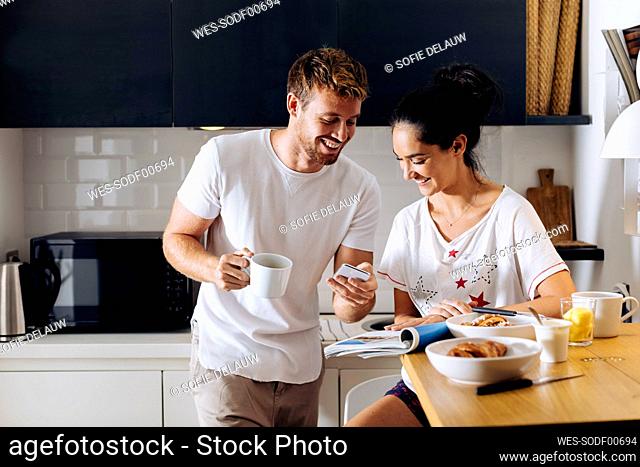 Happy young couple in the kitchen looking at cell phone