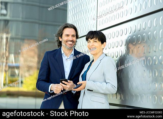 Smiling business people with mobile phone at metal wall