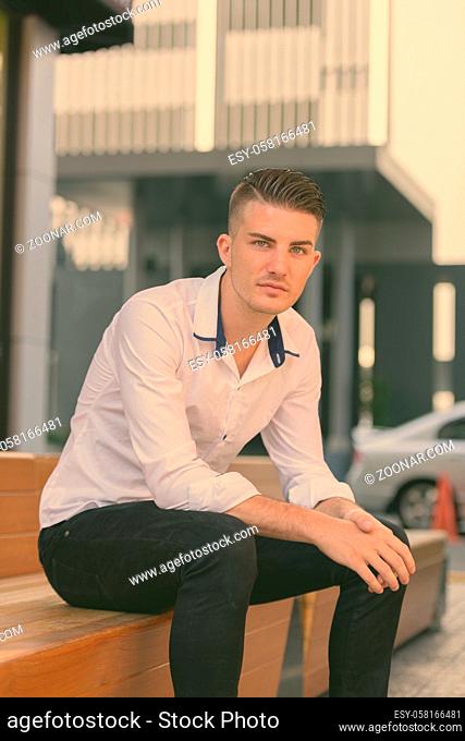 Young handsome man sitting on wooden stairs outside modern house