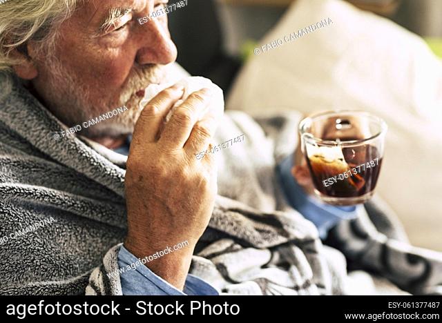 One old senior man with cold flu influenza symptoms drinking medicine or natural herbal tea at home to heal. Concept of virus and mature elderly people with...