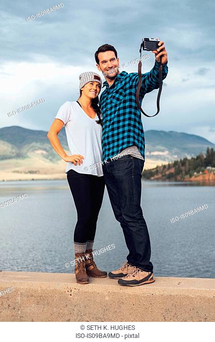 Couple standing on wall beside Dillon Reservoir, taking selfie, using camera, Silverthorne, Colorado, USA