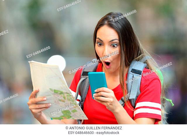Surprised teen tourist holding a map and reading online content in a smart phone on the street