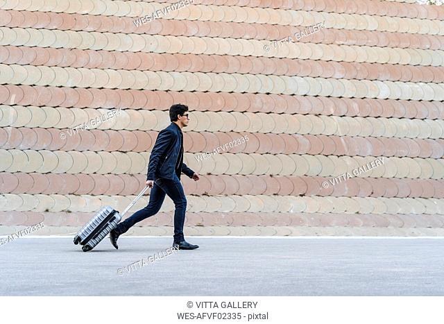 Running young businessman with rolling suitcase