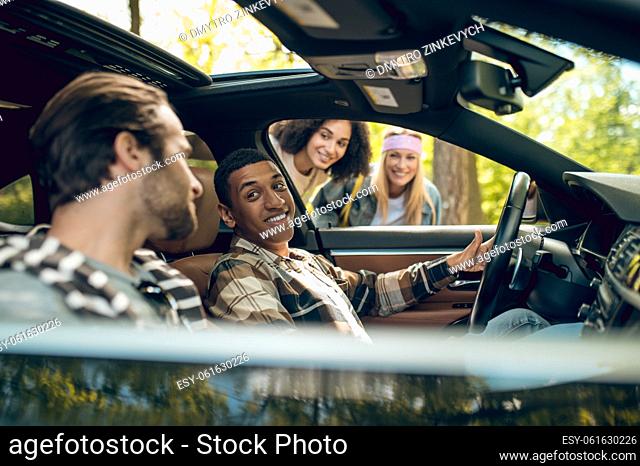 Hitchhikers. Smiling men in a car talking to girls on the road