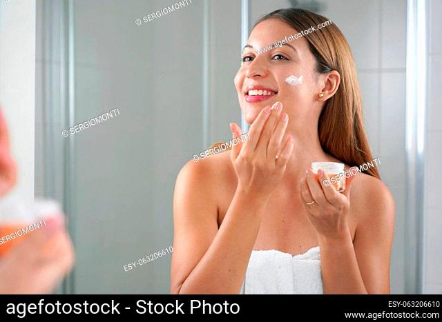 Skincare woman applying cream on her cheek. Face moisturizing nourishing invigorating treatments. Enjoying relaxing time