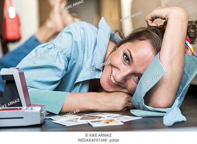 Portrait of happy young woman lying on the floor with instant photos