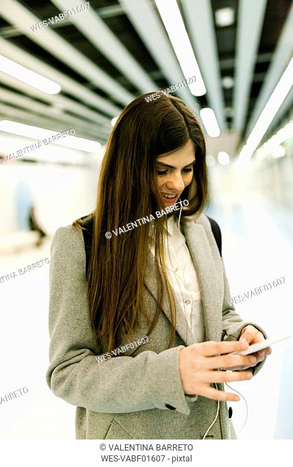 Smiling young woman using cell phone and earphones