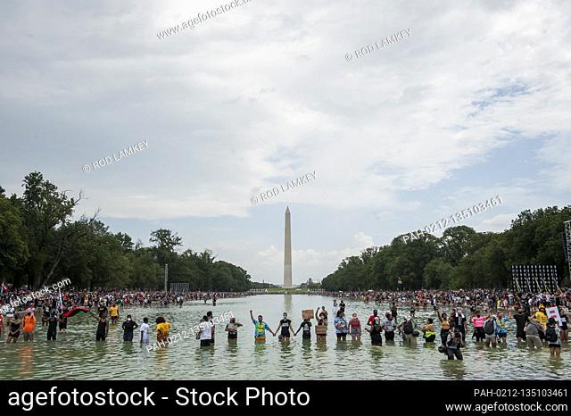 People stand in the cool water of the Reflecting Pool and join hands across the water, during the “Get Your Knee Off Our Necks” March on Washington at the...