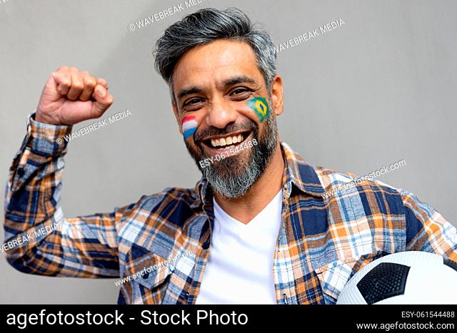 Portrait of happy biracial man with football and flags of netherlands and brazil on cheeks