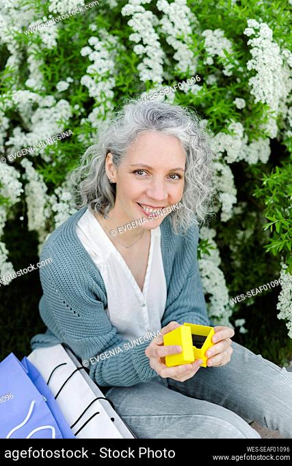 Happy woman holding yellow gift box in front of plant