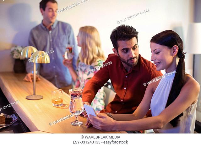 Couple interacting with each other while using mobile phone at bar counter