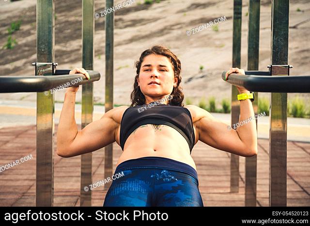 girl trains outdoors in street gym. Training of biceps and triceps. woman parallel bars workout exercise. female athlete exercising on parallel bars