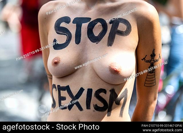 10 July 2021, Berlin: A participant of a bicycle demonstration under the motto ""No Nipple is free until all Nipples are free!"" has the writing Stop Sexism on...