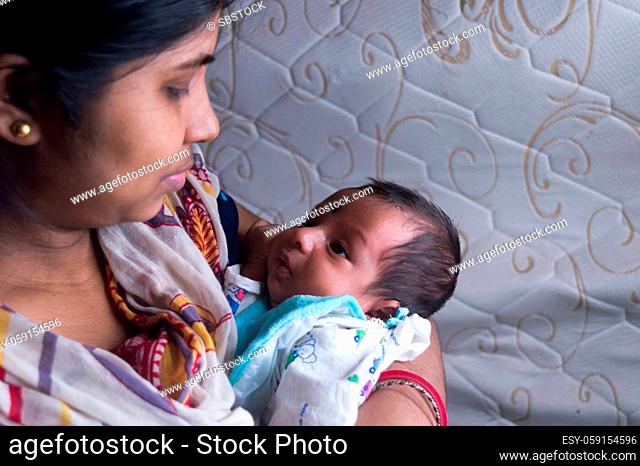 Close up face of a cute newborn baby boy happily looks at his mother in her mother lap. One month old Sweet little infant toddler. Indian ethnicity