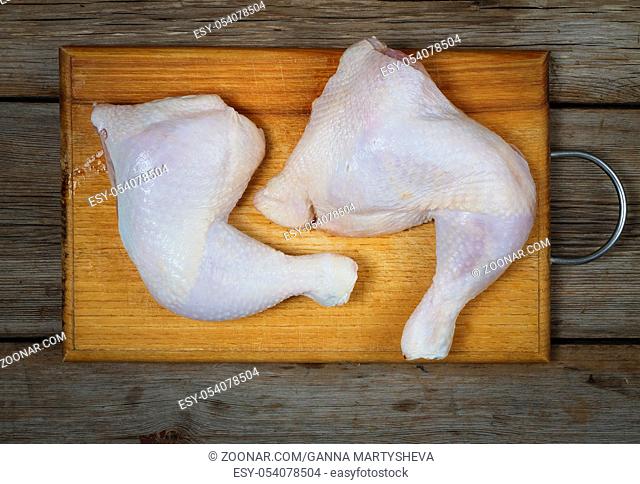 Raw uncooked chicken legs on a wooden cutting board , meat with ingredients for cooking. top view