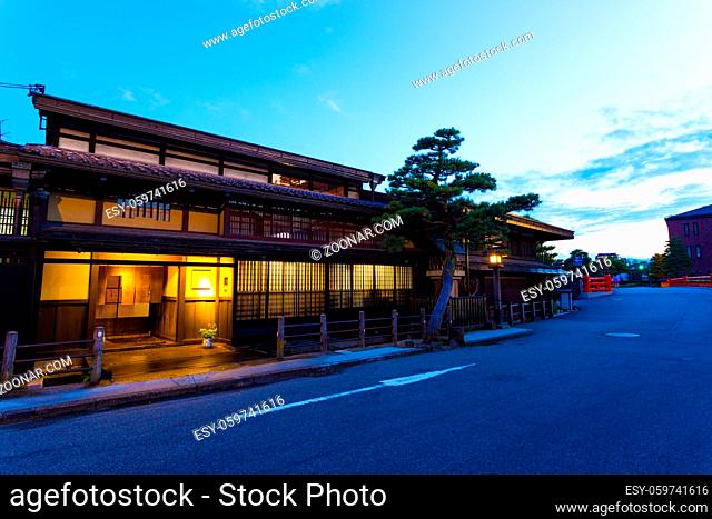 Modern street runs over Naka-bashi bridge in front of traditional Japanese wooden homes lighted at evening dusk in historic old town of Hida-Takayama in Gifu...