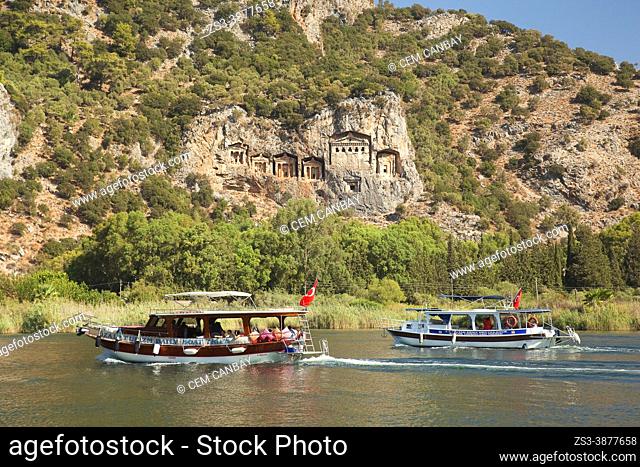 Touristic river boats between reeds on Dalyan River with the Lycian rock cut royal tombs of ancient Kaunos city at the background, Dalyan, Mugla Province