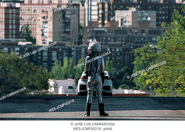 Rear view of boy dressed as an astronaut standing on a street in the city