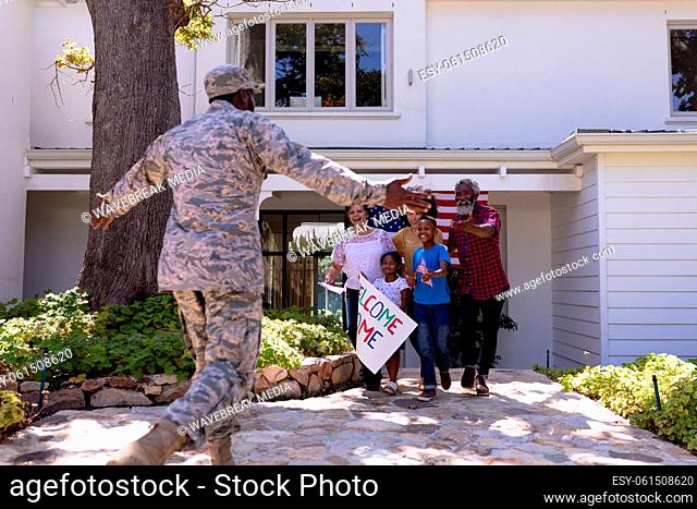 Multi-generation mixed race family welcoming an African American man wearing military uniform