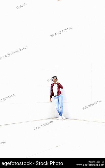 Smiling young woman leaning on white wall with legs crossed