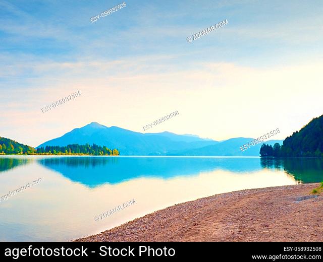 Romantic sunset at mountain lake. Stony beach and dark mountains in water mirror. Evening after heavy rainy day. Poor lighting conditions