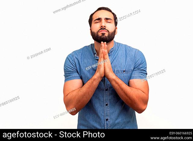 Deeply religious bearded man folding hands in prayer, closing eyes and talking to god, asking for help, expressing gratitude