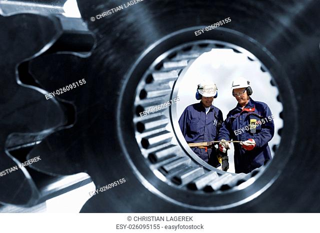 two mechanics, workers seen through a large cogwheels and gears machinery