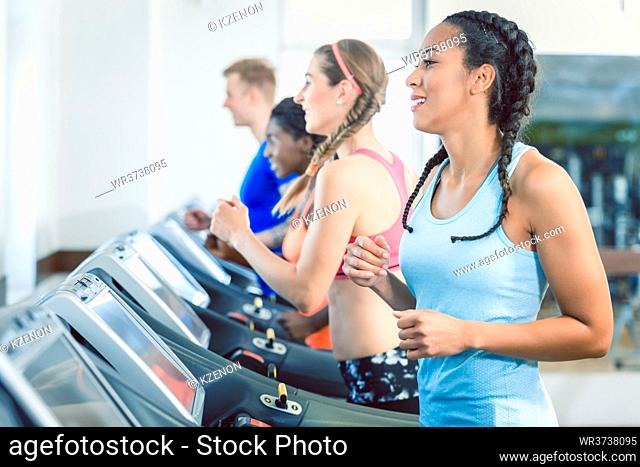 Side view of a fit happy woman and her training group on treadmill in the gym