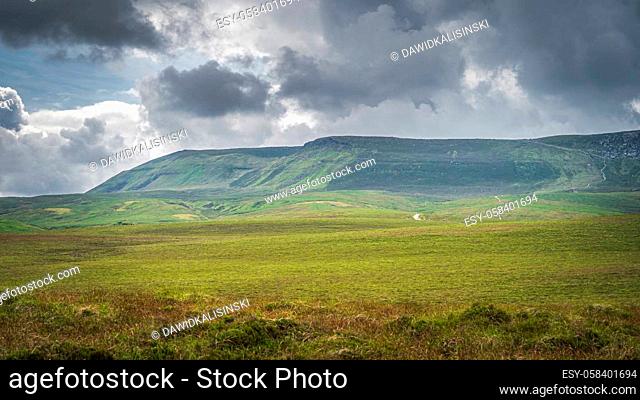 Green meadow and peatbog with a view on wooden boardwalk leading to Cuilcagh mountain, stormy, dramatic sky in background, Northern Ireland
