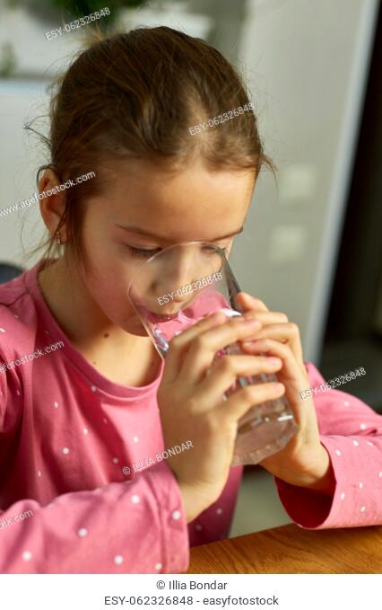 Close up of happy little girl drinking glass fresh water in kitchen, child recommend daily dose of clean aqua, dehydration, healthy lifestyle concept