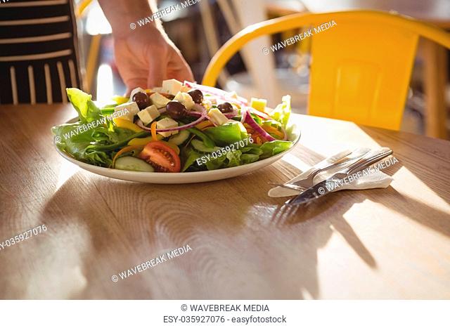 Cropped hand of waiter serving salad on table