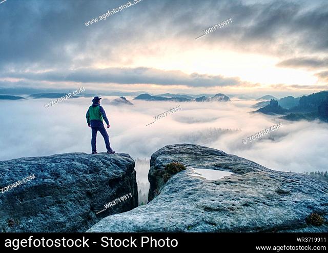 Male hiker finnaly standing on a rock stock and enjoying foggy mountain view
