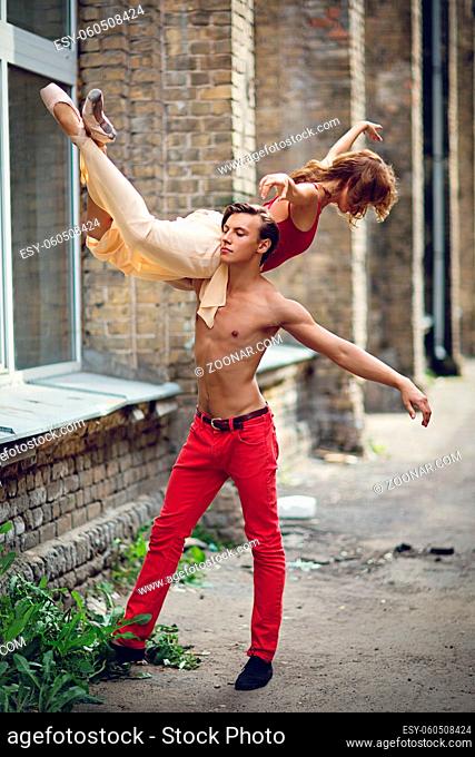 Beautiful young couple of modern ballet dancers dancing in street near old damaged building. Outside shot