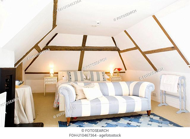 Wide-striped blue+white sofa in attic bedroom with lighted lamps on bedside tables